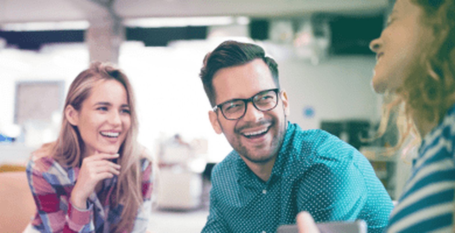 3 Personen sitzen gemeinsam lachend am Tisch