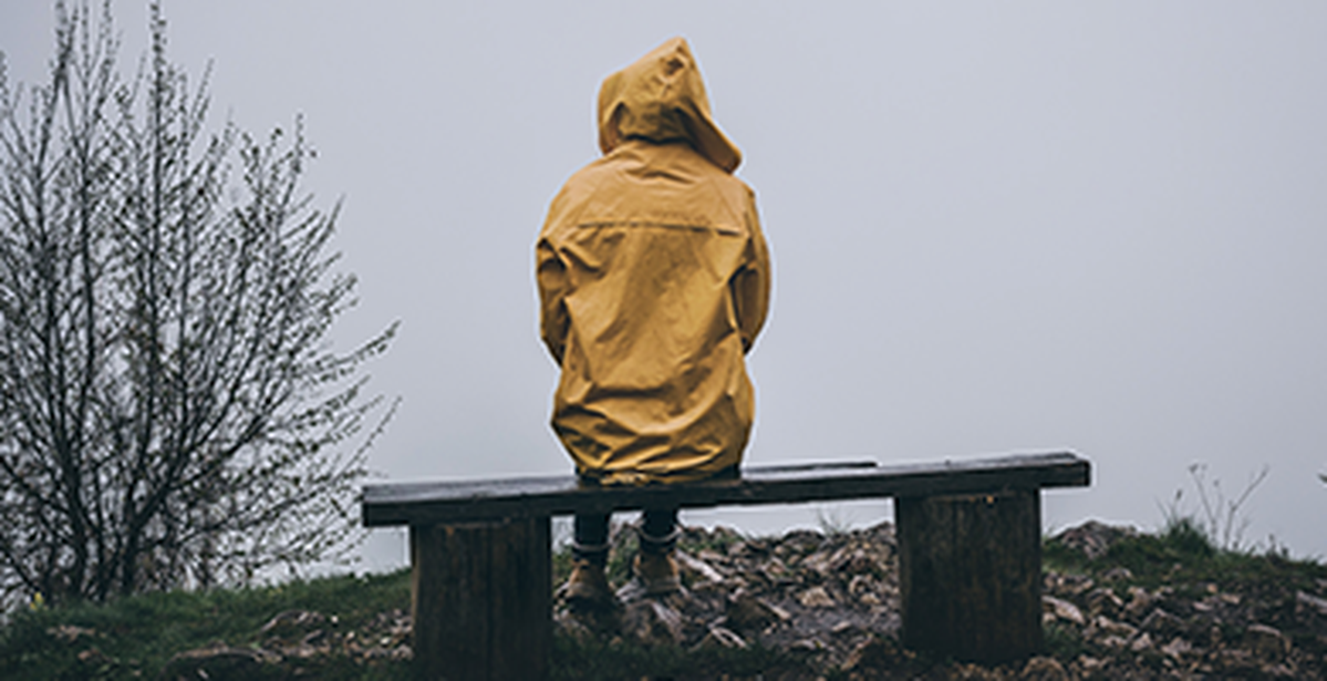 Eine Person sitzt bei regnerischem Wetter alleine auf einer Bank